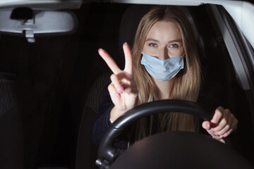 Young woman in a protective mask driving a car