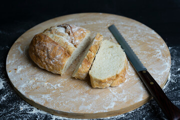 Sliced wheat bread with flour and knife on wooden board.Dark food background.