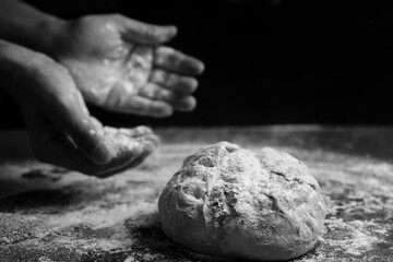 Bread baking concept.Hands with flour and traditional bread on floury table.Black and white image with copy space.