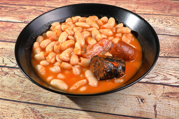 Asturian bean stew in black plate on rustic wooden table