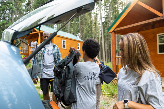 Family Unpacking Car Outside Cabin At Summer Camp