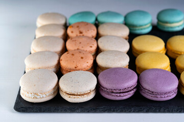 Macarons are laid out on a black slate in beautifully colored rows.