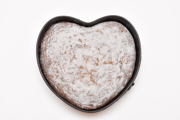top view of freshly baked heart shaped cake in springform pan and dusted with powdered sugar on a white background