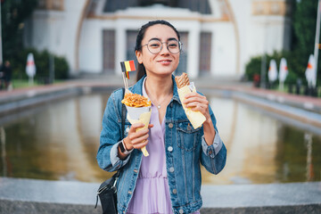 Happy Asian woman enjoying refreshing beverages and eating Belgian fries while looking at the camera