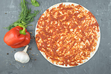The base of the dough with ketchup and pizza ingredients, on the table. Cooking pizza. Tomato paste is smeared on the pizza base.