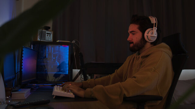 Male using PC and concentrating while wearing white headphones in a darkened room