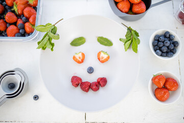 Smiling face made with berries and mint leaves on a plate