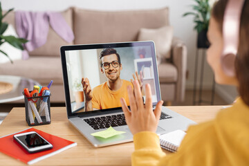 Little girl using headphones and laptop for learning online class from school teacher by remote...