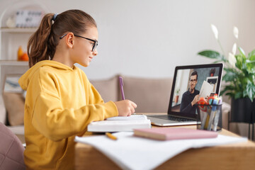 School girl having video conference with online teacher on laptop in living room at home....