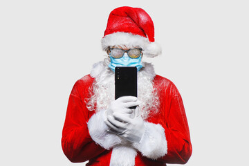 Portrait of Santa Claus in respiratory protection mask stands on free background with smartphone in...