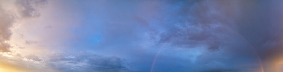 Summer sunset after rain sky panorama with fleece purple clouds and rainbow. Evening dusk good weather natural cloudscape background.