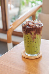A glass of iced latte fusion two layers matcha and chocolate on wooden table,  homemade latte refreshment in cafe background.