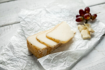 Solid piece of cheese with tap grapes on a wooden background.