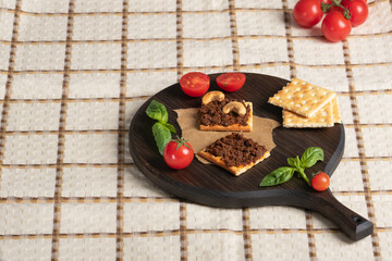 square crispbread crackers with vegetable pate on  round dark cutting board. Cherry, cashew and...