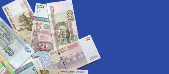 Photo of somoni bank notes from Tajikistan and Russian ruble bank notes on blue background. Banner size, copy space. Focus on money