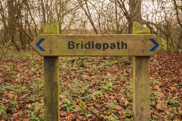 A wooden bridleway sign indicates the direction of the path in woodland