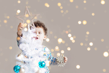 Little boy in pijamas decorating white Christmas tree