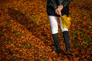 Graceful woman feet in elegant boots walking on fall leaves in an autumn forest