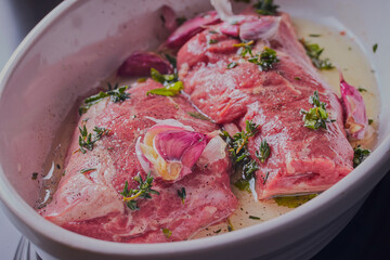 Lamb steaks marinating in dish with herbs.