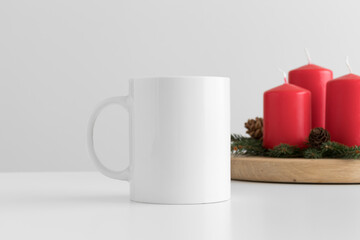 White mug mockup with candles on a table. Christmas decoration
