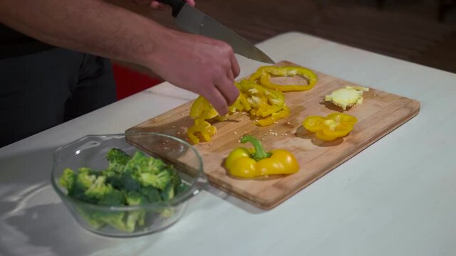 Black adult man slicing a yellow bell pepper on a bambu cutting board