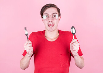 Hungry man holds a fork and spoon in his hands and thinks about delicious food over pink background . Diet and meal concept.