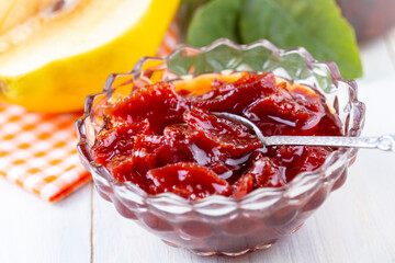 Homemade quince jam in a glass jar on an old wooden background. Fresh quince fruits and leaves and quince jam.