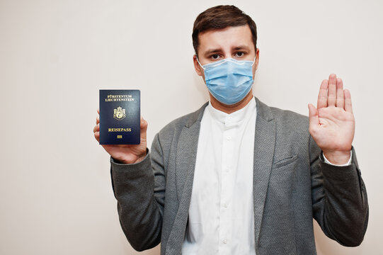 European man in formal wear and face mask, show Liechtenstein passport with stop sign hand. Coronavirus lockdown in Europe country concept.