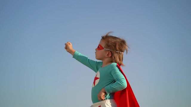 Superhero child against blue sky background. Slow motion