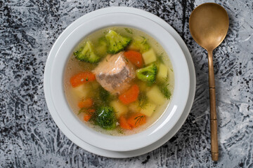 Fresh salmon fish soup with carrots, potatoes and onions in a white plate, close up. Top view