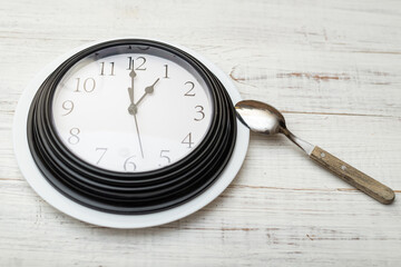 Lunch time clock. Classic watch and spoon on a white wooden background.