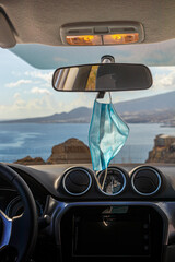 Surgical mask hanging from the rearview mirror of the car, parked at the sea