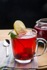 Berry tea in a cup with lemon on a napkin next to a spoon.