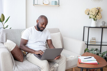 Working atmosphere at home. African-American man wearing a white T-shirt with a laptop focuses on online marketing course. People, online education and technology concept.