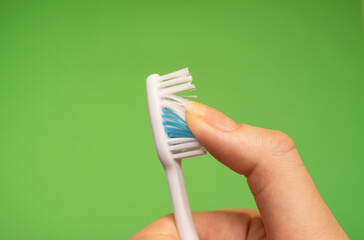 Blue Toothbrush in woman's right hand against a green background with fingers guided through the...