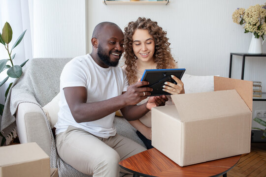 Having settled down comfortably at home on the sofa, the future mommy and her husband joyfully consider the printed photo brought by the courier in the box. Pregnancy, family and joy concept.