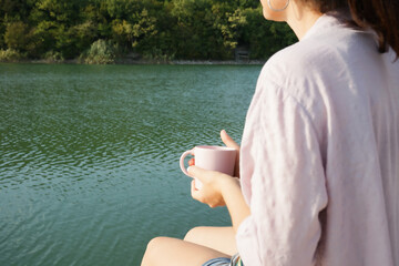 a woman drinks coffee on a pier by the lake