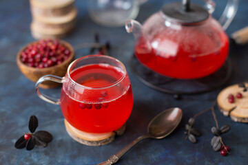 Hot cranberry tea in a glass Cup and a teapot on a dark cold background. Warming and healing tea with berries. New year's drink for a cozy evening.