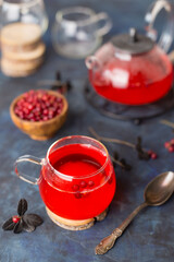 Hot cranberry tea in a glass Cup and a teapot on a dark cold background. Warming and healing tea with berries. New year's drink for a cozy evening.