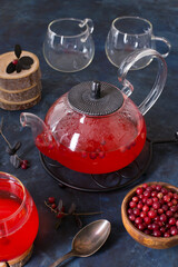 Hot cranberry tea in a glass Cup and a teapot on a dark cold background. Warming and healing tea with berries. New year's drink for a cozy evening.