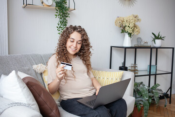 Pretty future mom loves shopping! Sitting at home on sofa in jeans and T-shirt, she orders everything she likes on the site, paying with card. Pregnancy, people, technology concept.