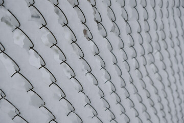 Metal fence mesh covered with snow. The gloomy morning after a snowfall. Selective focus. Copy space.