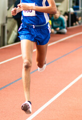 Runner racing on an indoor track in a blue uniform