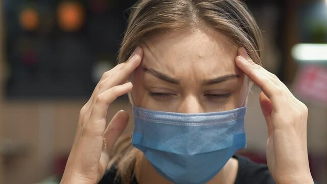 Sick woman in medical protective face mask close-up. She is not feeling well and has a headache, she massaging head
