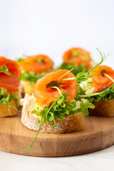 Canapes with mozzarella cheese, salad, salmon and pea sprouts, toast with red fish on a wooden board close up