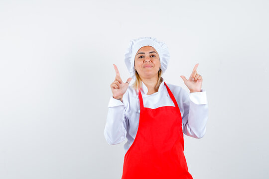  Young Woman Pointing Up In Red Apron And White Hat And Looking Happy. Front View.