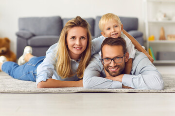 Happy young family relaxing on warm rug in living room of their newly bought house