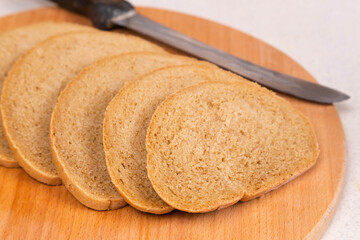 Sliced bread with a knife on a wooden chopping board. Top view