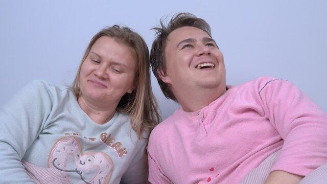 Married couple wearing pajamas lies in bed and listens to child or someone else tells ridiculous stories. They look at each other questioningly and start laughing at absurdity of what is happening.