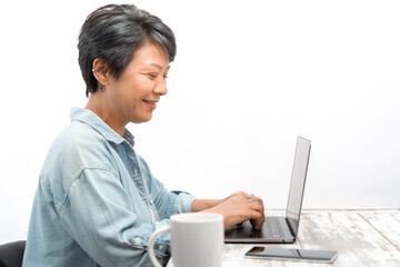 Senior Designer woman working or shopping online on a laptop in office. Asian mature female looking and smiling at the laptop computer while sitting at her desk. Elderly online technology concept